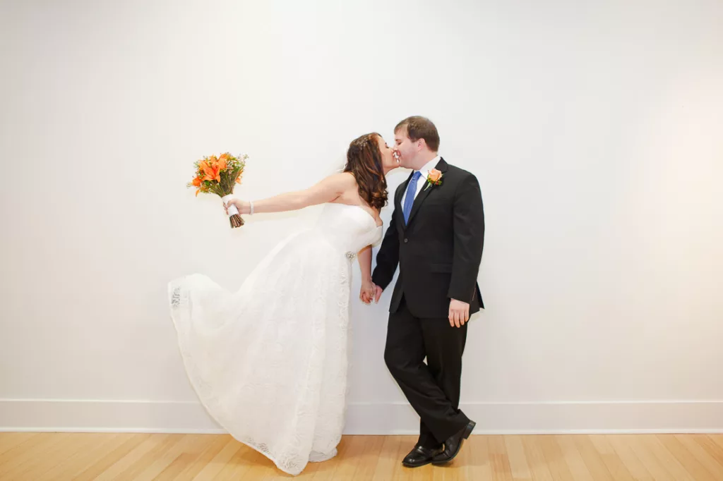 A bride and groom kissing in front of a white wall at VisArts.