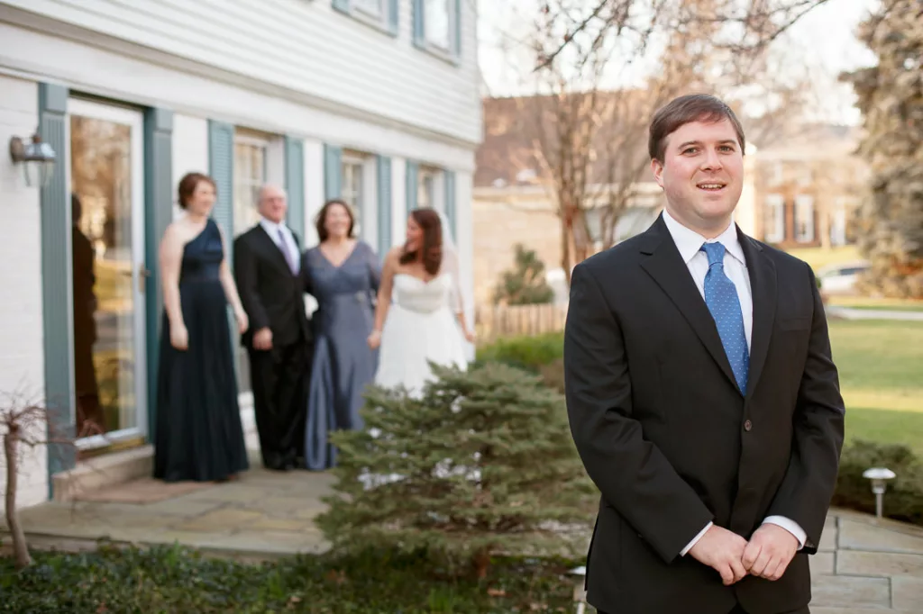 A groom in a suit standing in front of a house.