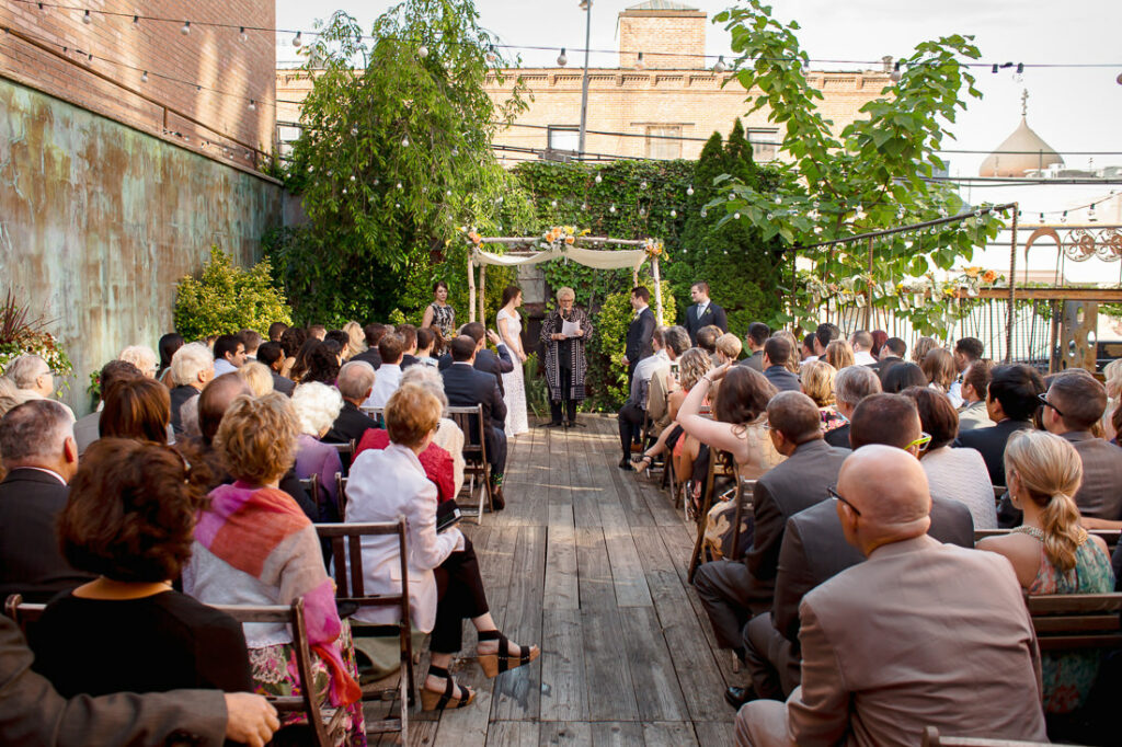A group of people sitting in chairs on a wooden deck during a wedding ceremony.