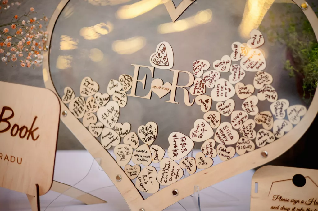 A wooden heart shaped book holder with names written on it at a wedding