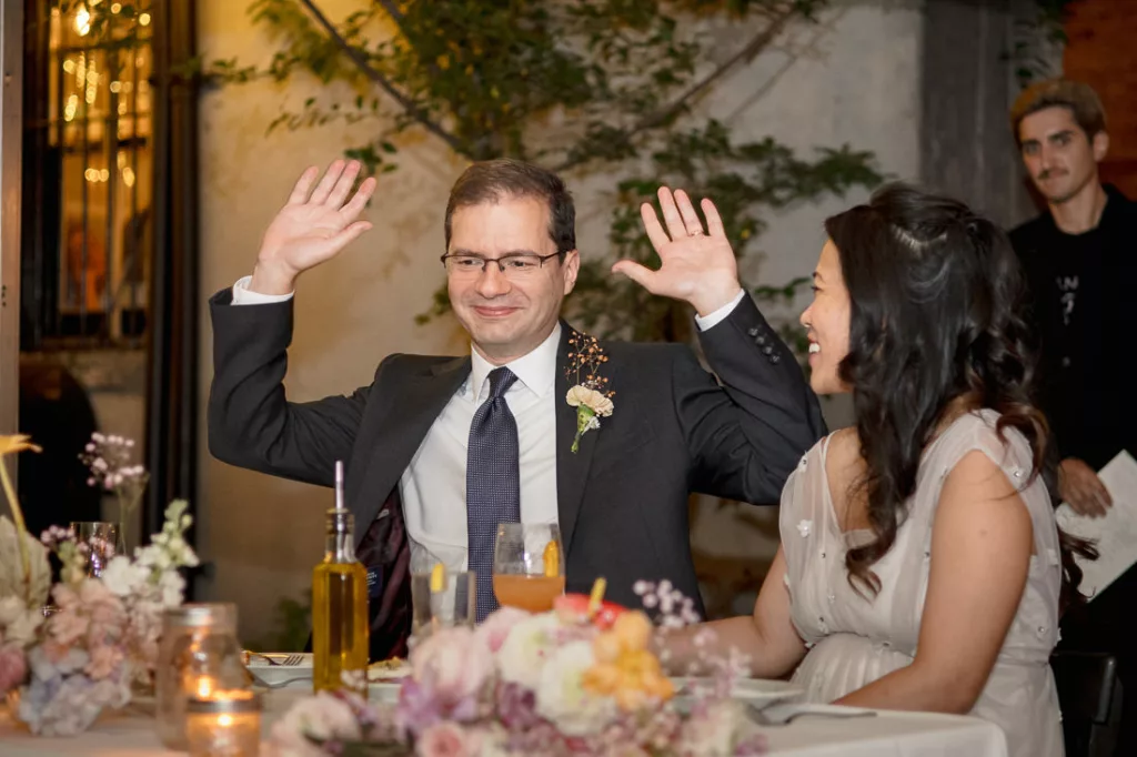A bride and groom waving their hands at a wedding reception.