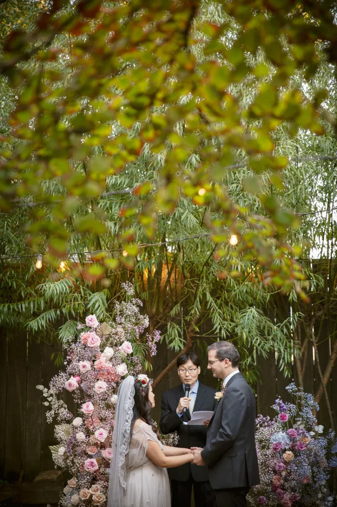 A bride and groom exchange vows under a canopy of flowers in the backyard of Frankies 457 Spuntino.