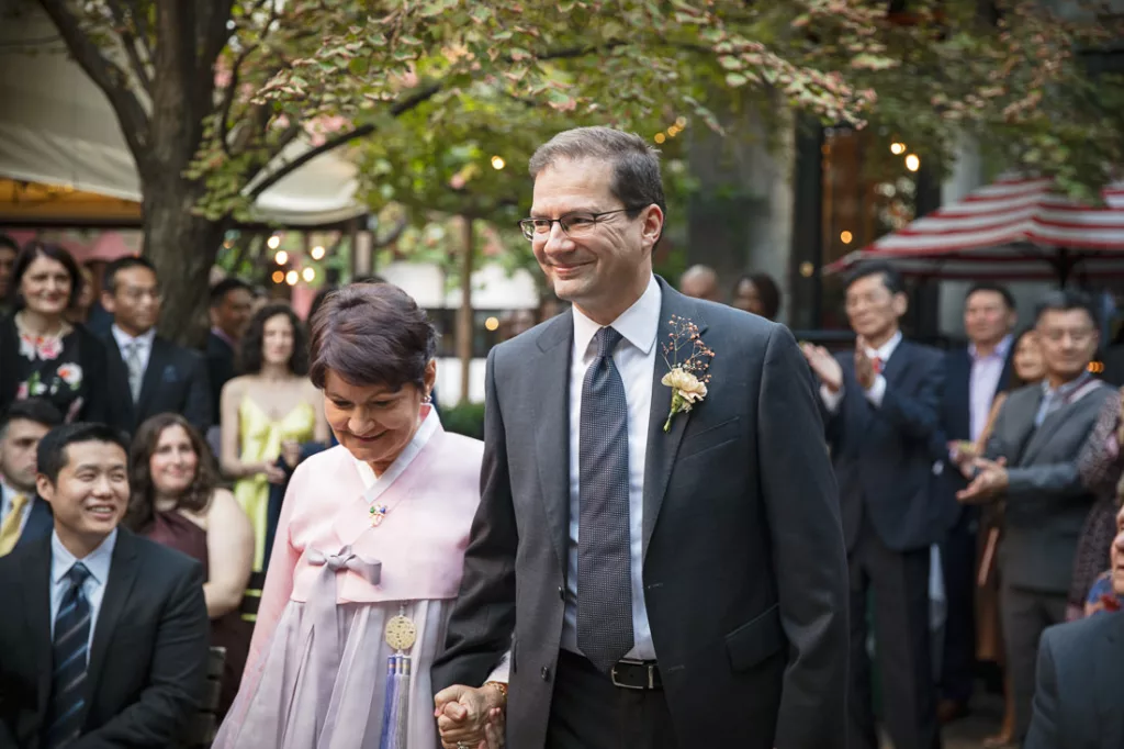 A groom and his mom walking down the aisle at a wedding.