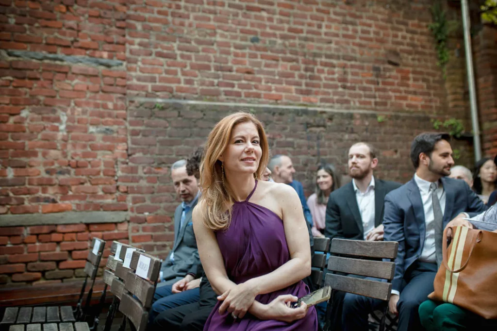 A woman in a purple dress sitting on a bench during a wedding ceremony.