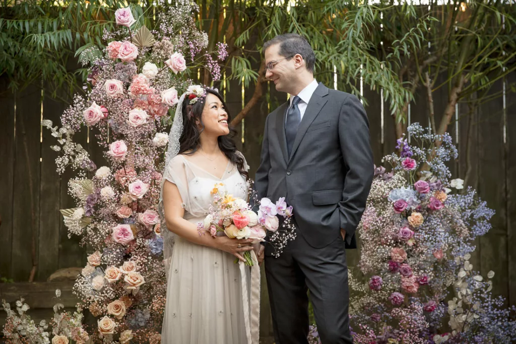 A bride and groom standing in front of a flower wall.