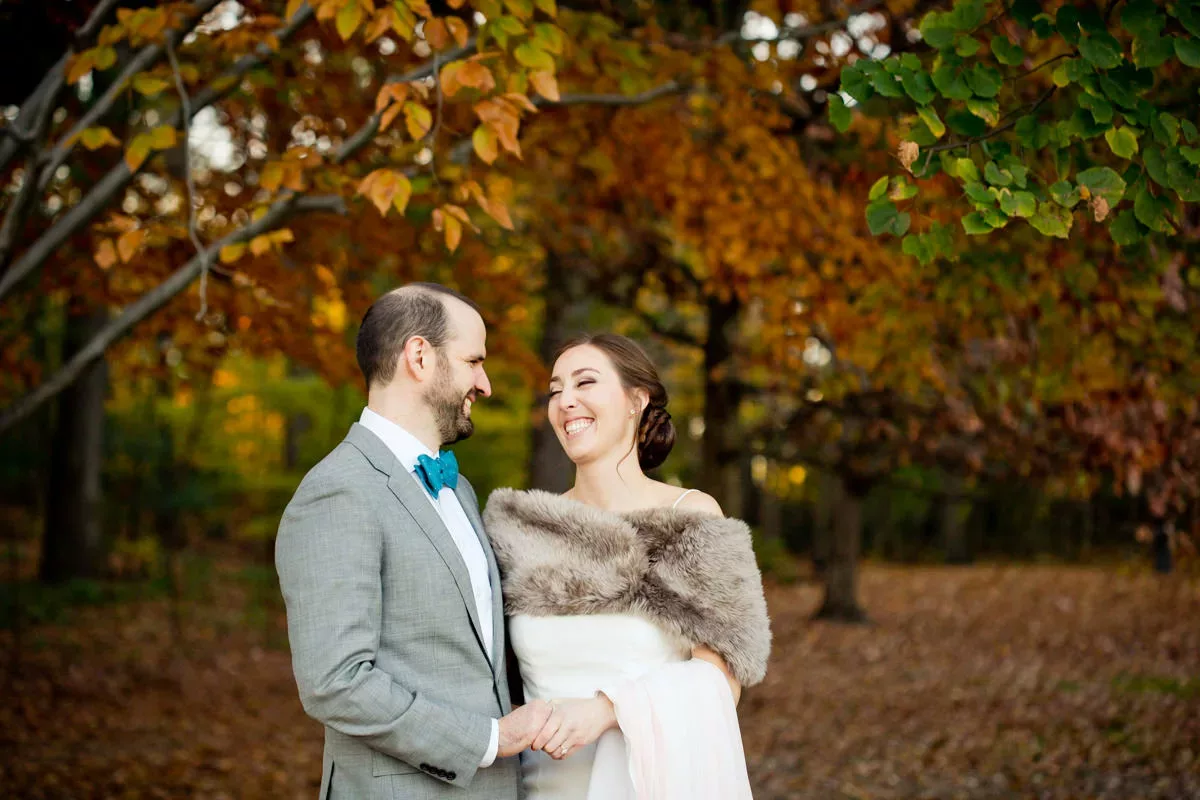 A bride and groom standing in the fall leaves.