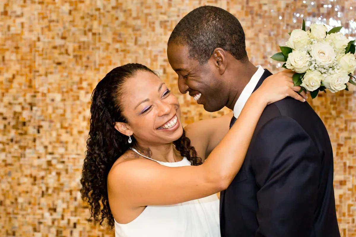 A bride and groom hugging in front of a tiled wall.