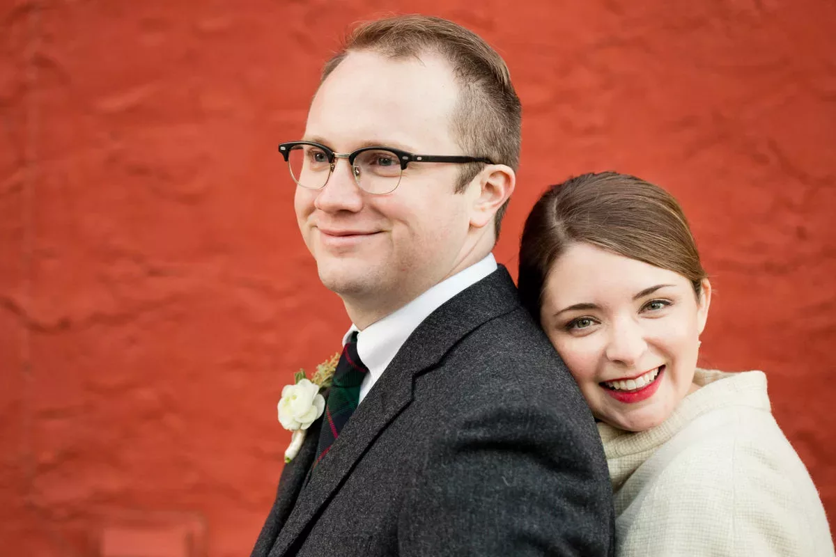 A bride and groom posing in front of a red wall.