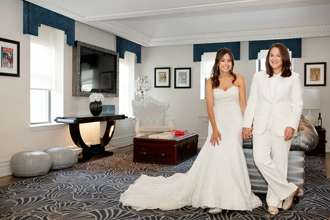 Two brides in white suits standing in a room during their wedding at the Manhattan Penthouse.