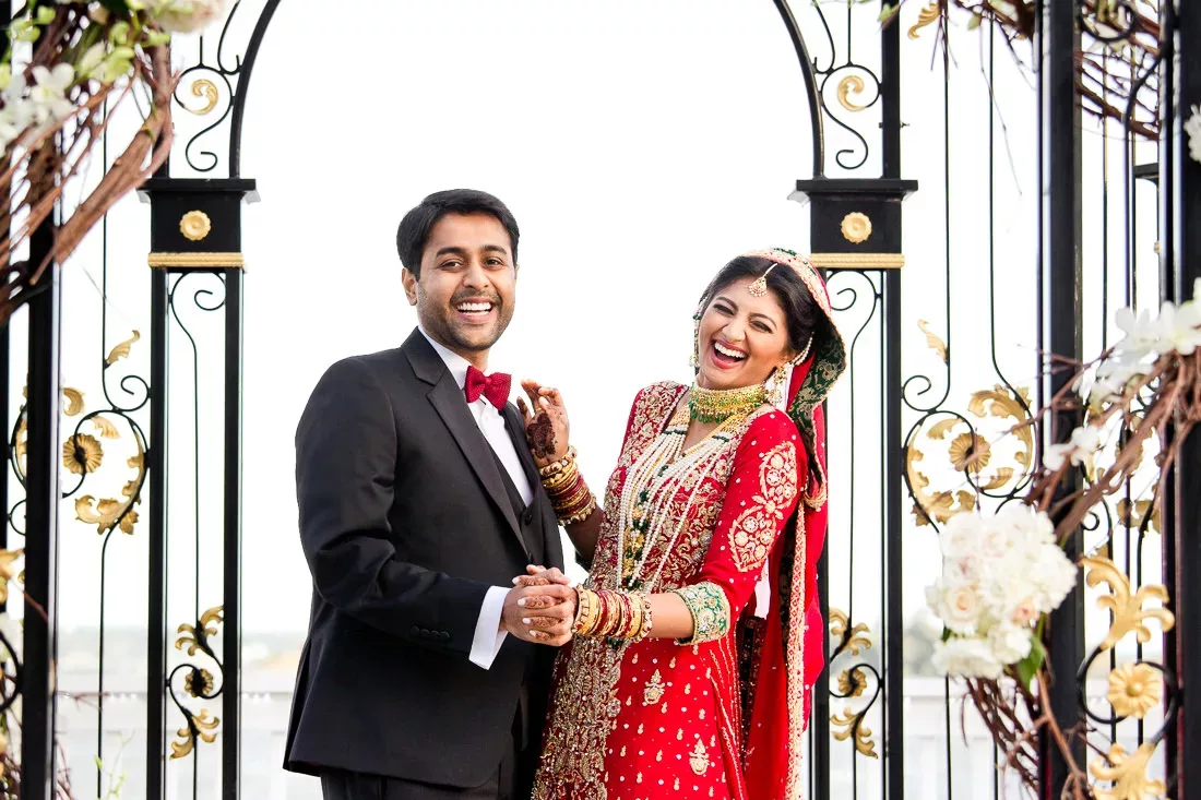 A bride and groom pose for a photo in front of an archway.