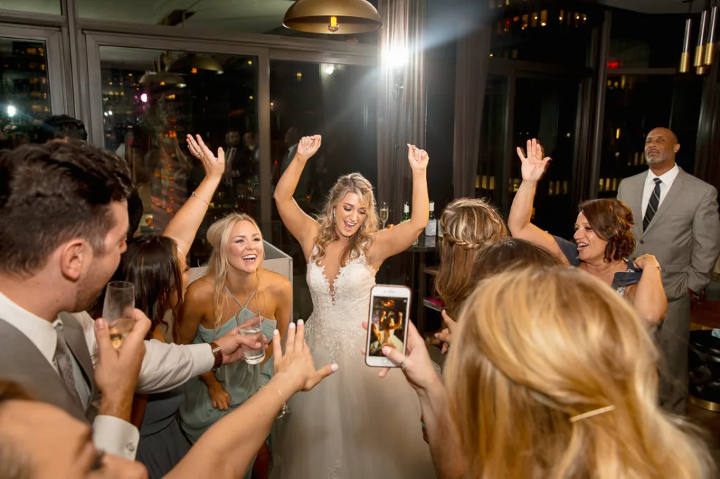 A bride in a white dress with her hands up in the air dancing.