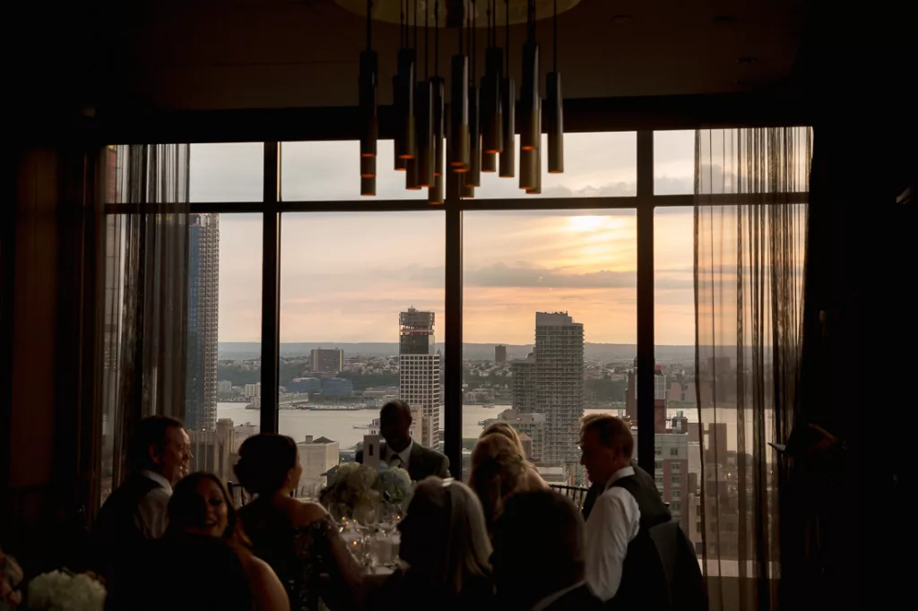 A group of people sitting at a table in front of a window with a view of the city at The Skylark in NYC.