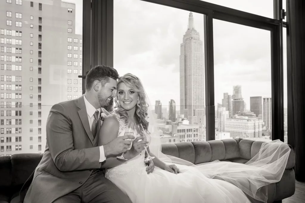 A bride and groom sitting on a couch with a view of the city.