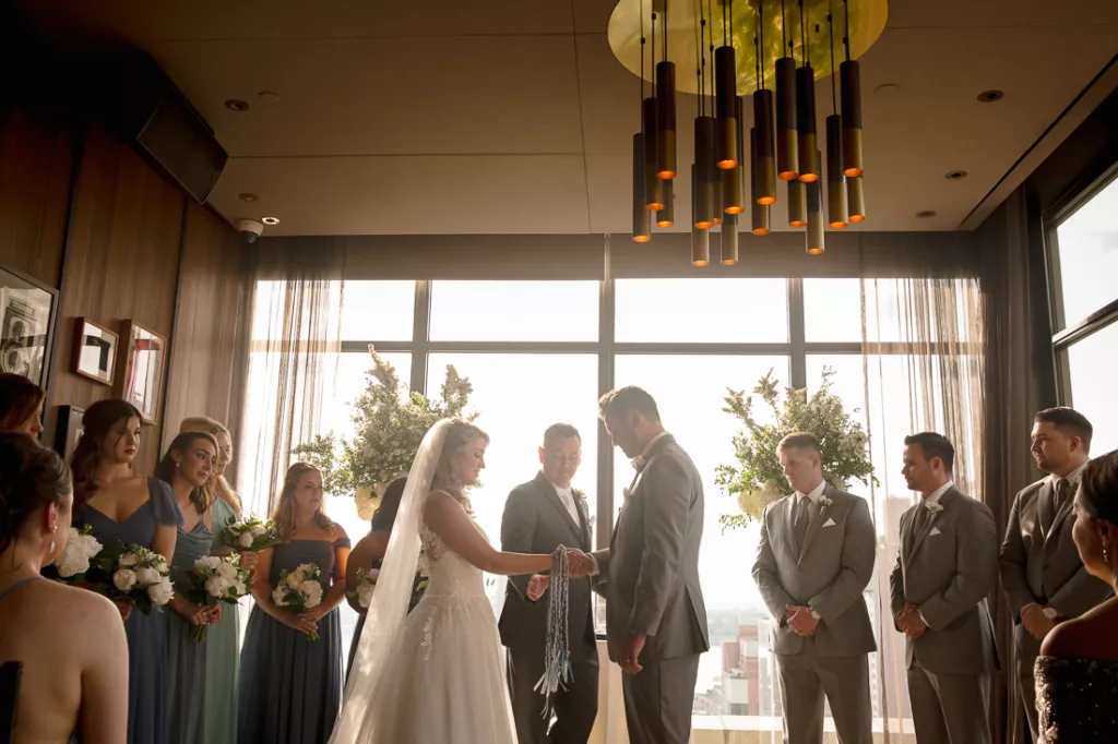 A bride and groom exchange vows in front of a large window.