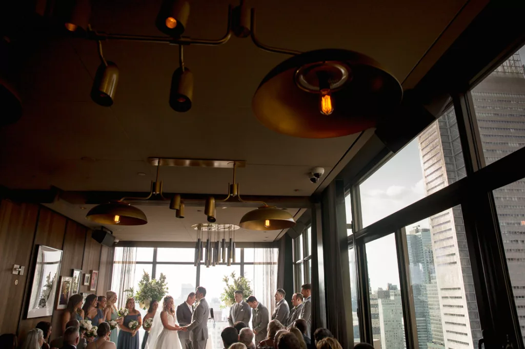 A group of people standing in a room with a window and a couple of people standing in front of them at The Skylark in NYC.