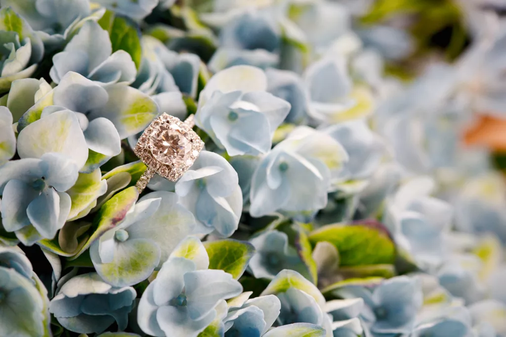 An engagement ring is surrounded by blue flowers.