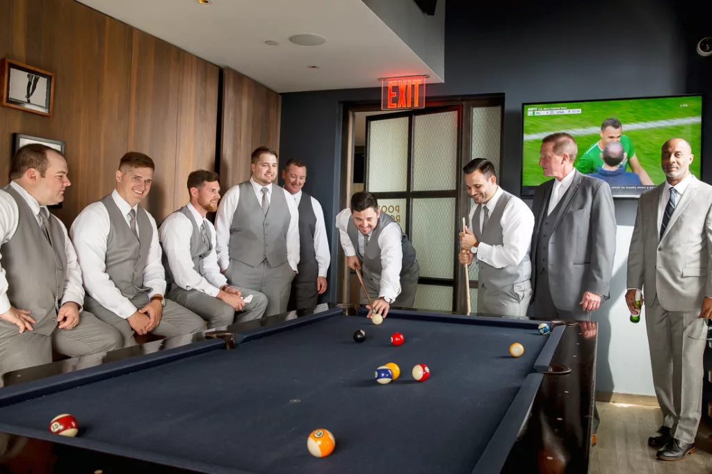 A group of groomsmen playing pool in a room.